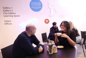 A photograph of two visitors sitting and drinking coffee in the Tate Liverpool + RIBA North cafe