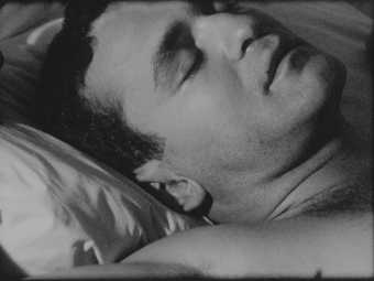 Still from black and white film showing a man sleeping